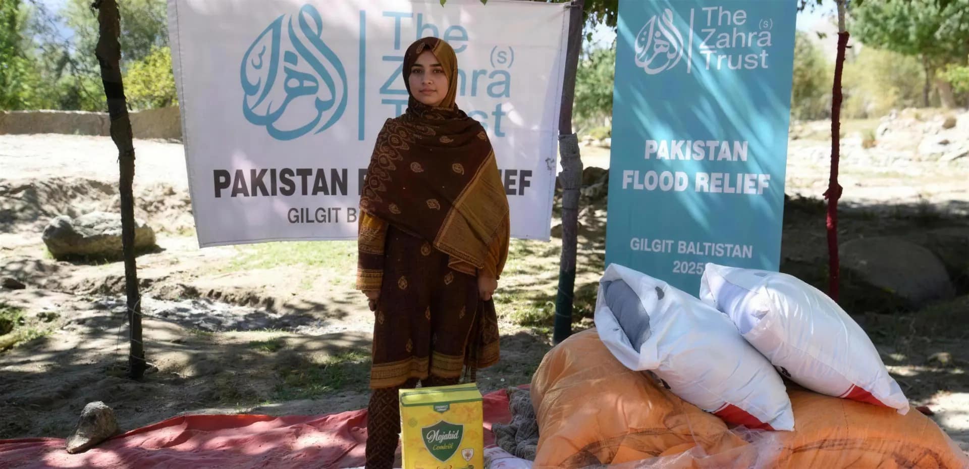 A woman stands before Pakistan flood relief banners with emergency food parcels and bedding in the foreground